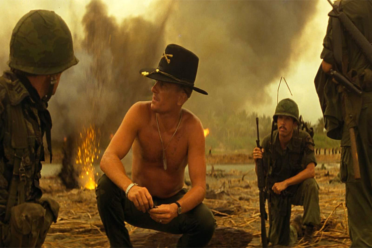 Robert Duvall (sem camisa) é militar surfista completamente pirado em Apocalypse Now.